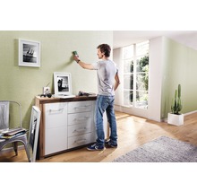 Ein Mann benutzt einen Detektor zum Anbringen von Bildern an einer Wand über einem Sideboard in einem Wohnzimmer.