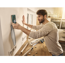 Mann benutzt ein Ortungsgerät an einer Wand in einer Küche, um eine Halterung anzubringen.