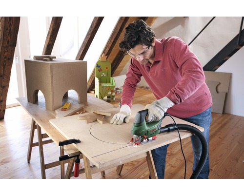Un homme découpe un trou dans une plaque de bois sur un établi à l''aide d''une scie sauteuse