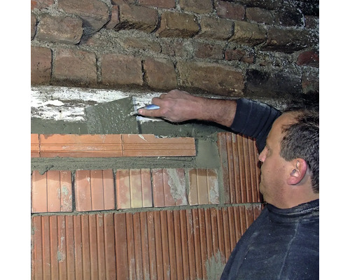 Un homme enduit un mur de briques avec du mortier et une truelle.