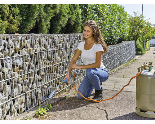 Femme en train d''enlever les mauvaises herbes avec un brûleur à gaz contre un mur de gabions