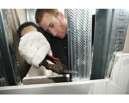 Un homme coupe un profilé métallique avec une cisaille à tôle pour la construction sèche.