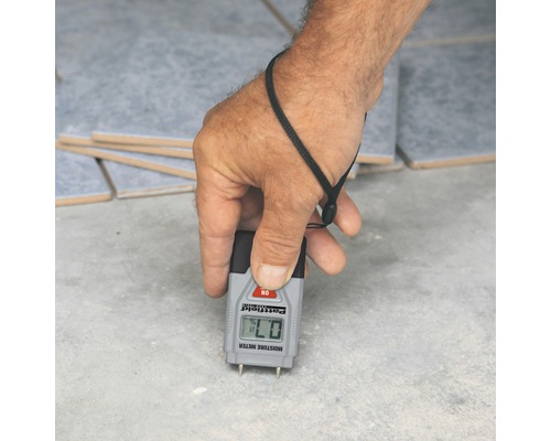 Eine Hand misst mit einem Feuchtigkeitsmesser die Feuchtigkeit eines Untergrunds.