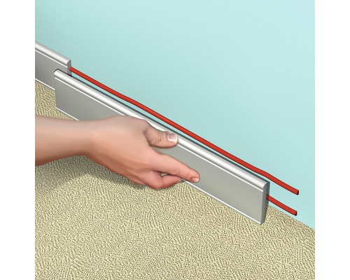 Personne montant une plinthe avec goulotte de câbles sur un mur