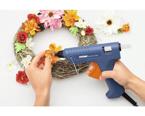 Une couronne décorative est ornée d''un pistolet à colle chaude et de fleurs artificielles.