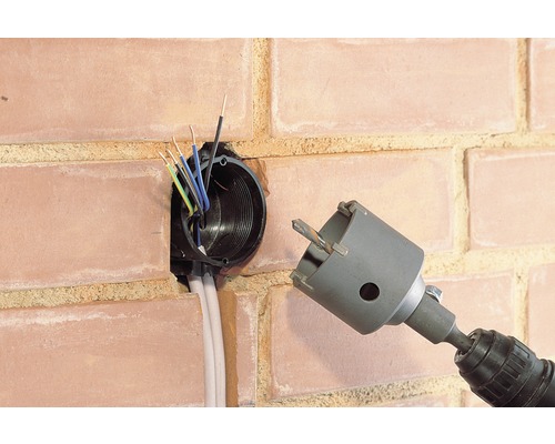 Une perceuse avec un embout de scie cloche perce un trou pour une boîte d''encastrement dans un mur de briques.