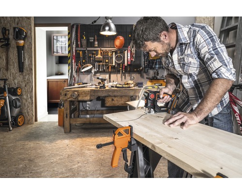 Homme sciant une planche de bois avec une scie sauteuse dans un atelier