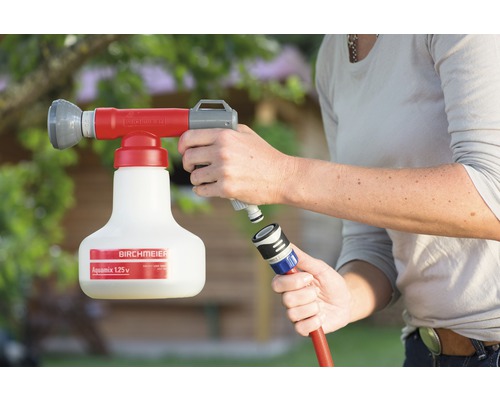 Une personne connecte un engrais Birchmeier Aquamix à un tuyau d''arrosage.