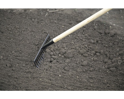 Gartenrechen mit Holzstiel im Einsatz auf Erde