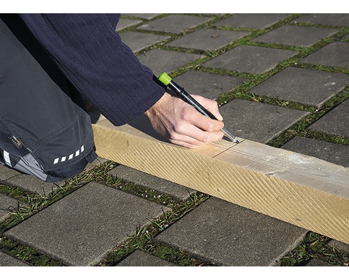 Eine Person zeichnet mit einem Zimmermannsbleistift eine Linie auf ein Holzbrett.