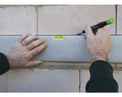 Eine Person benutzt eine Wasserwaage und einen Stift, um eine Linie auf einer Wand zu markieren.