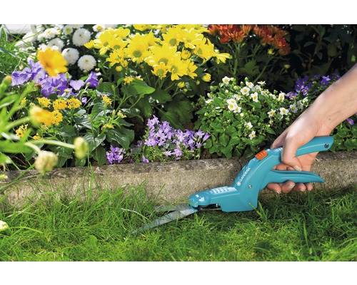 Person schneidet Rasen mit einer Gardena Grasschere vor einem Blumenbeet.