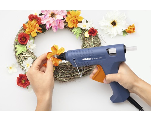 Une couronne de fleurs décorative est ornée avec un pistolet à colle chaude