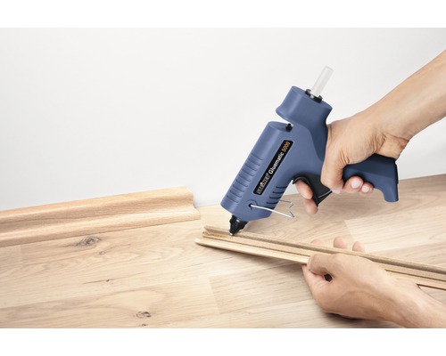 Une personne colle des moulures décoratives avec un pistolet à colle chaude.