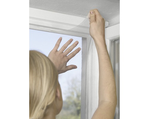 Person befestigt ein Fliegengitter an einem Fensterrahmen