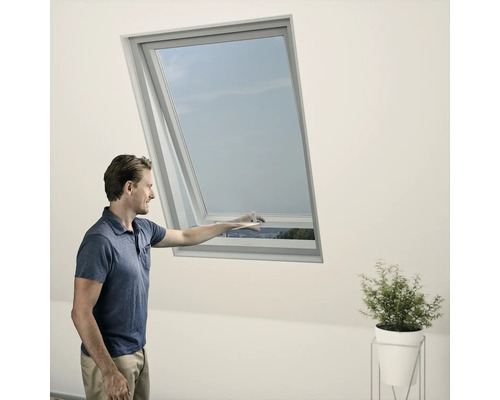 Ein Mann öffnet ein Dachfenster in einem hellen Raum.