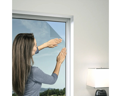 Frau bringt Sonnenschutzfolie an einem Fenster an