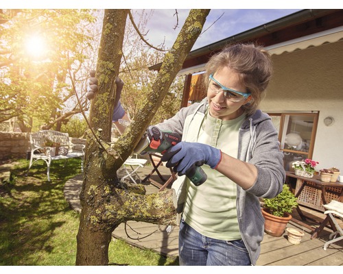 Femme coupant un arbre avec une scie à branches sans fil dans le jardin