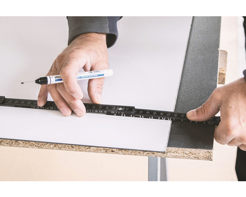 Une personne marque une plaque avec un stylo et un mètre pliant.