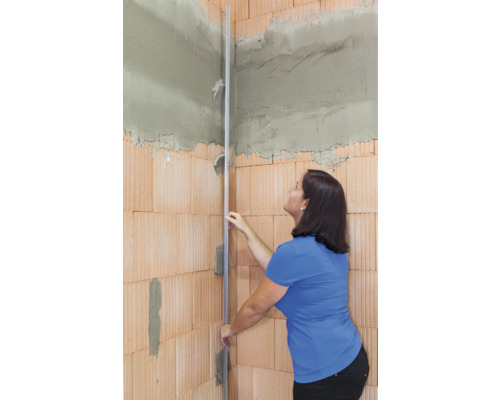 Frau mit Richtscheit an einer mit Ziegeln gemauerten Ecke eines Raumes