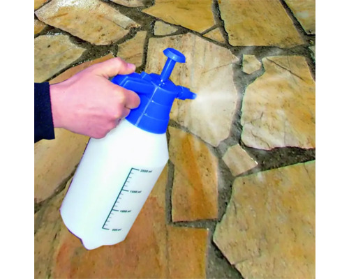 Une main actionne un pulvérisateur à pression sur des dalles de pierre.