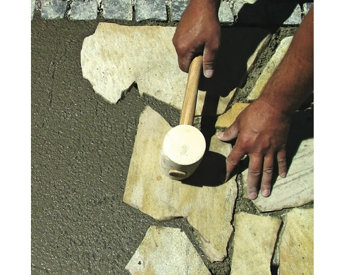 Eine Person verlegt Natursteine mit einem Gummihammer.