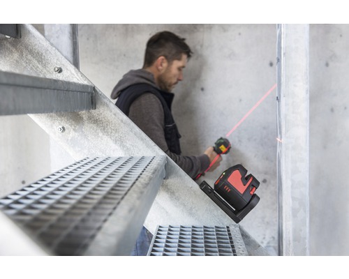 Artisan utilisant un laser linéaire sur un escalier métallique pour l''alignement sur un mur.