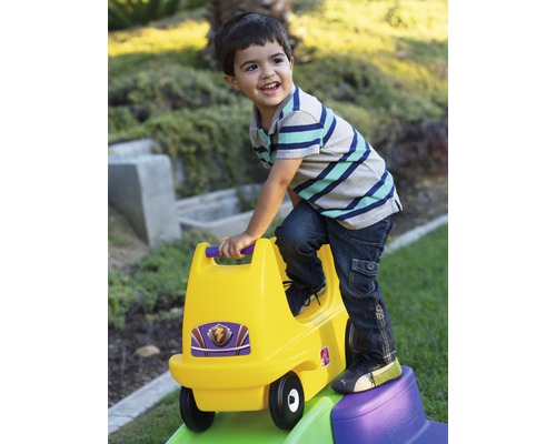 Kind spielt mit gelbem Rutschauto im Garten