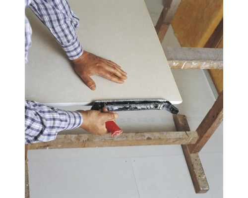 Un homme lisse une plaque de plâtre avec un rabot à arêtes sur un tréteau en bois