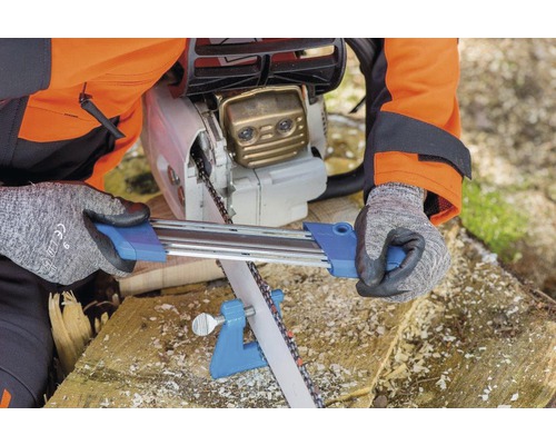 Une personne affûte une tronçonneuse avec un affûteuse sur un morceau de bois.