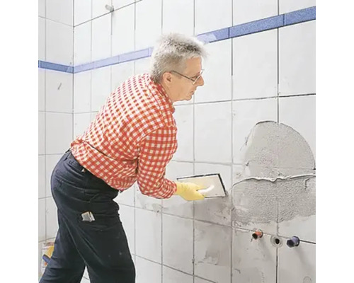 Un homme applique du mortier-colle sur un mur de salle de bains.