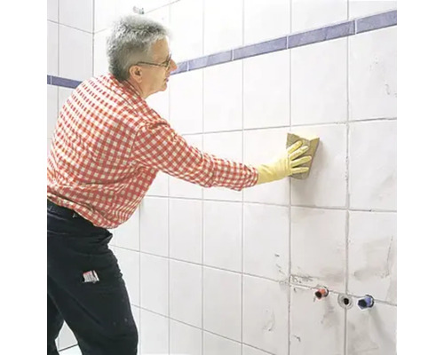 Un homme nettoie des carreaux avec une éponge dans la salle de bain.