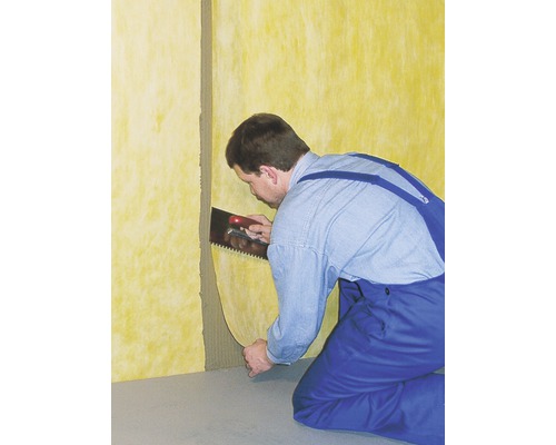 Ein Mann befestigt eine Dämmplatte mit einer Kelle an einer Wand.