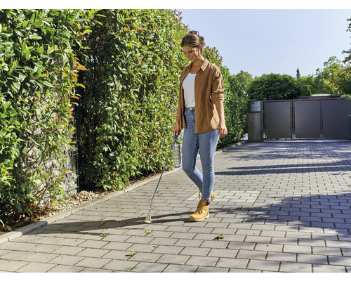 Frau entfernt Unkraut mit einem Unkrautstecher auf einem gepflasterten Weg