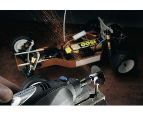 Logo Dremel. Une personne travaille une pièce avec un outil multifonction Dremel, des étincelles jaillissent. Une voiture miniature est visible en arrière-plan.