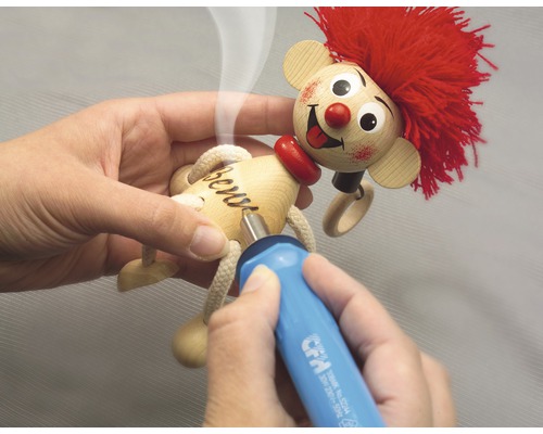 Person brennt mit einem Brennkolben den Namen in eine Holzpuppe.