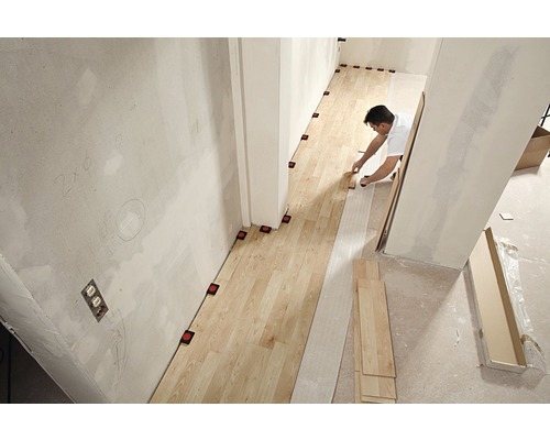Un homme pose un plancher en bois dans une pièce avec des aides au nivellement.