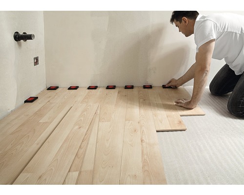 Homme posant un sol stratifié avec des entretoises contre le mur