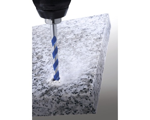 Eine Bohrmaschine bohrt mit einem Steinbohrer ein Loch in eine Steinplatte.