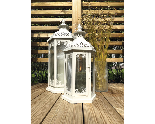 Deux lanternes blanches en métal et en verre sur une terrasse en bois, à côté d''un vase en verre avec des fleurs séchées