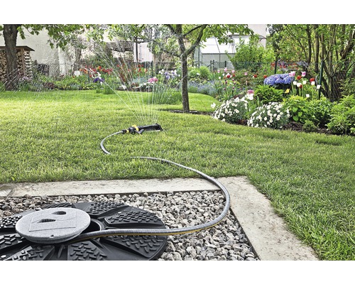 Rasensprenger im Einsatz in einem Garten mit Blumenbeeten und Bäumen