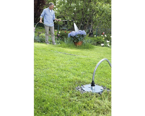 Mann bewässert Blumen mit einem Gartenschlauch und einer Wassersteckdose im Garten