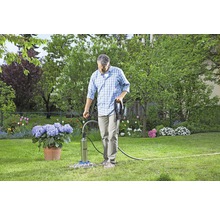 Un homme utilise une pompe de puits profond dans le jardin, entouré de fleurs et d''espaces verts.