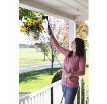 Une femme arrose des fleurs suspendues avec une douchette de jardin.