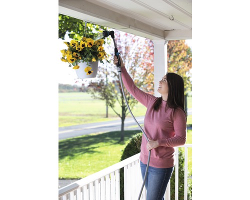 Une femme arrose des fleurs suspendues avec une douchette de jardin.