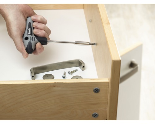 Hand schraubt Möbelgriff mit Schraubendreher an Schublade