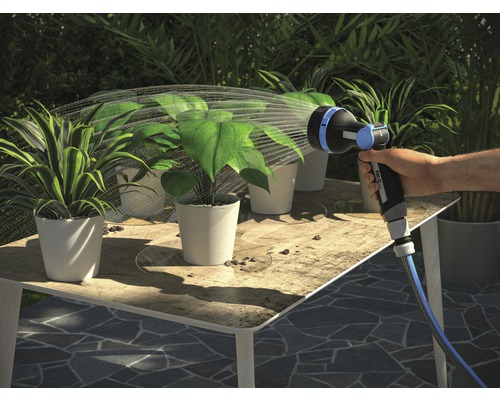 Une main arrose des plantes avec un embout de tuyau d''arrosage sur une table.