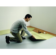 Un homme pose un isolant phonique dans une pièce avec un sol stratifié.