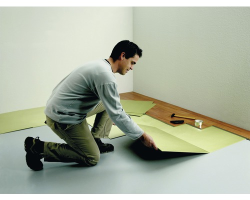 Un homme pose un isolant phonique dans une pièce avec un sol stratifié.