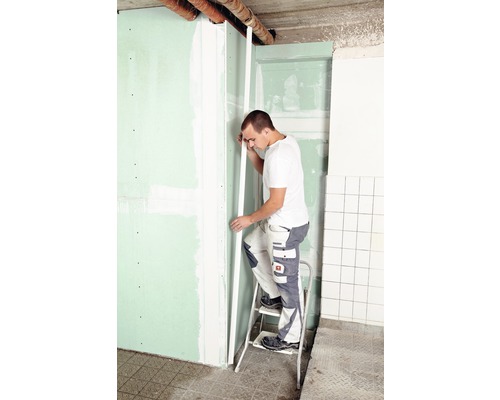 Mann auf einer Leiter, der eine Gipskartonplatte an einer Wand befestigt